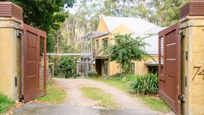 A gated entrance with a gravel path leading to a building with a sloped roof. - Tanglin - Mount Macedon (Mount Macedon)