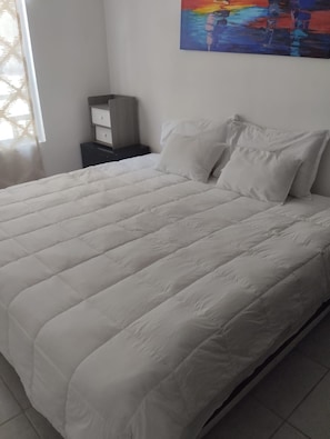 A bed with white bedding, a nightstand with drawers, and a painting on the wall. - 4-bedroom townhome in lovely Puerto Morelos with AC and jacuzzi for 8 (Puerto Morelos)