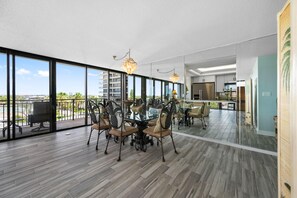 A spacious dining area with a glass table and chairs, large windows, and a view of the city. - Mansions By The Sea 406b - Premier (Treasure Island)