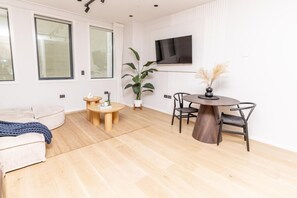A modern living room with a sofa, a round wooden table with chairs, a potted plant, and a flat-screen TV mounted on the wall. - Luxury & Style in the Heart of Auckland Opp Train Station (Auckland CBD)