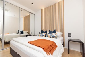 A modern bedroom with a large bed, a mirror, and a wooden panel wall. - Luxury & Style in the Heart of Auckland Opp Train Station (Auckland CBD)