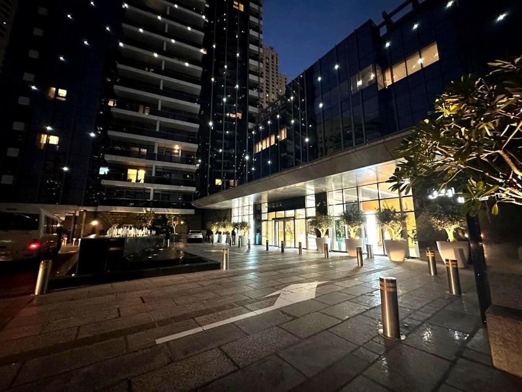 A modern building with a glass facade, a courtyard with a water feature, and potted plants.