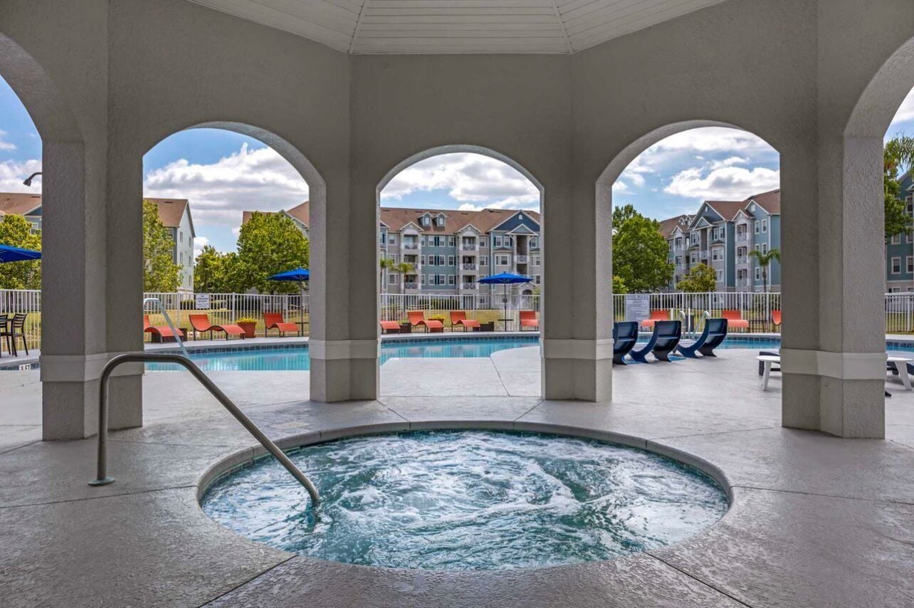 A pool area with a hot tub, lounge chairs, and a view of multi-story buildings.
