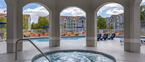 A pool area with a hot tub, lounge chairs, and a view of multi-story buildings.