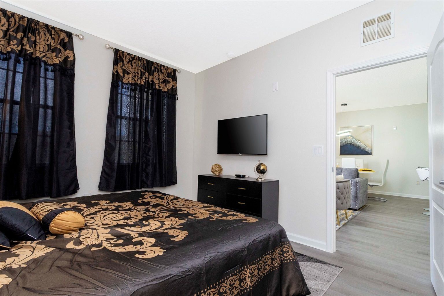 A bedroom with a bed, a TV, a dresser, and a door leading to another room.