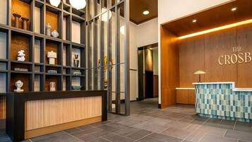 A reception area with a wooden reception desk, a tiled wall with a mosaic pattern, and a modern shelving unit with various decorative items.