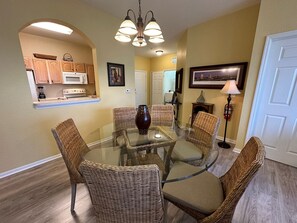 A dining area with a glass table surrounded by wicker chairs, a vase, and a chandelier. - 3BR Windsor Hills Near Disney + Water Park (Kissimmee)