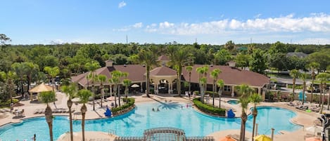 A resort with a large central pool, palm trees, and a covered pavilion.
