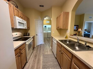 A compact kitchen with wooden cabinets, a microwave, stove, and a sink. - 3BR Windsor Hills Near Disney + Water Park (Kissimmee)