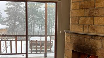 A room with a fireplace, a sliding glass door leading to a snowy deck, and a brown sofa.
