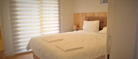 A hotel room with a bed, a nightstand, a lamp, and a window with blinds.