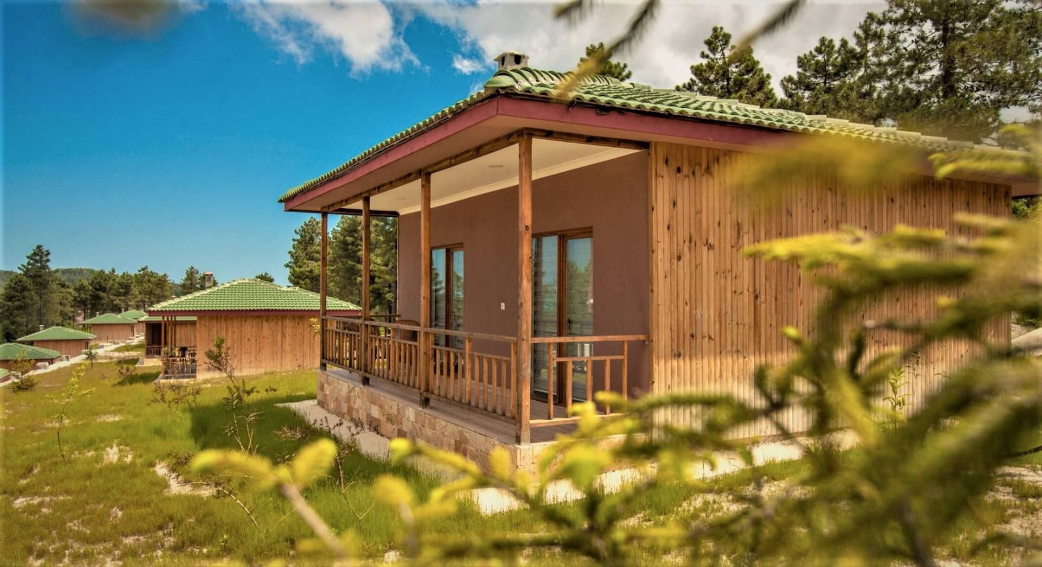 Una cabaña de madera con balcón, rodeada de vegetación y otras cabañas.