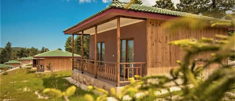 A wooden cabin with a balcony, surrounded by greenery and other cabins.