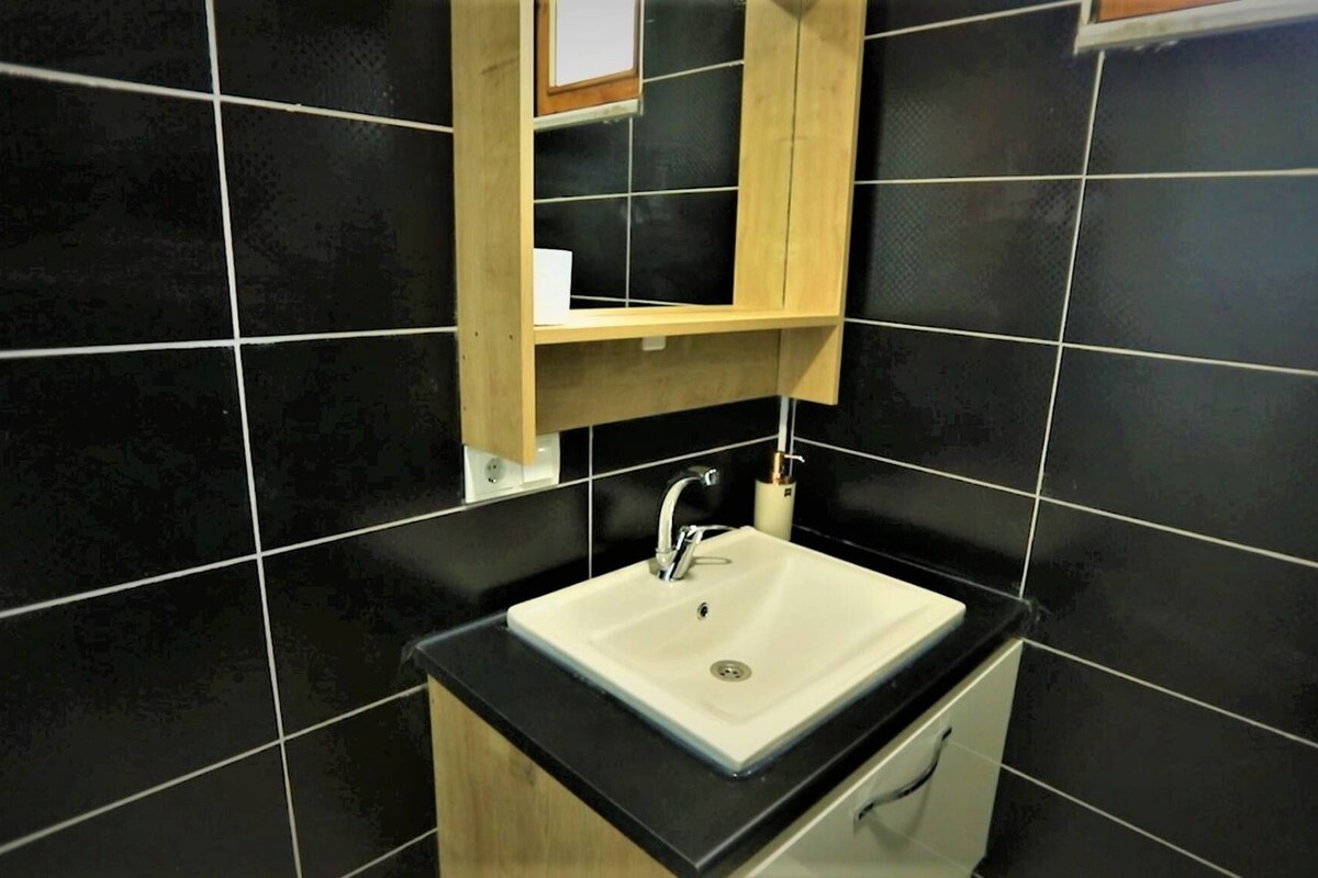 A bathroom with a white sink, black tiles, and a wooden cabinet above the sink.