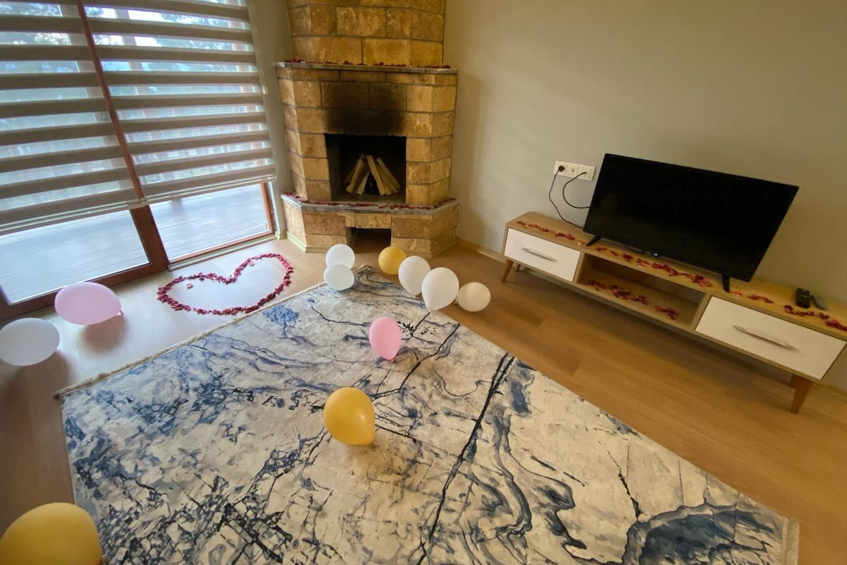 A living room with a stone fireplace, a flat-screen TV, and a marble-patterned rug.
