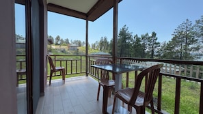 A balcony with a table and chairs, a view of a grassy area and trees, and a building in the background. - Ultra-luxury Villa for Rent 00012 (Ünye)