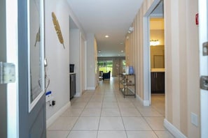 A hallway with a tiled floor, a door on the left, and a dining area with a table and chairs visible in the background. - Luxury 8BR Family Home Near Disney at Encore 54MA (Kissimmee)