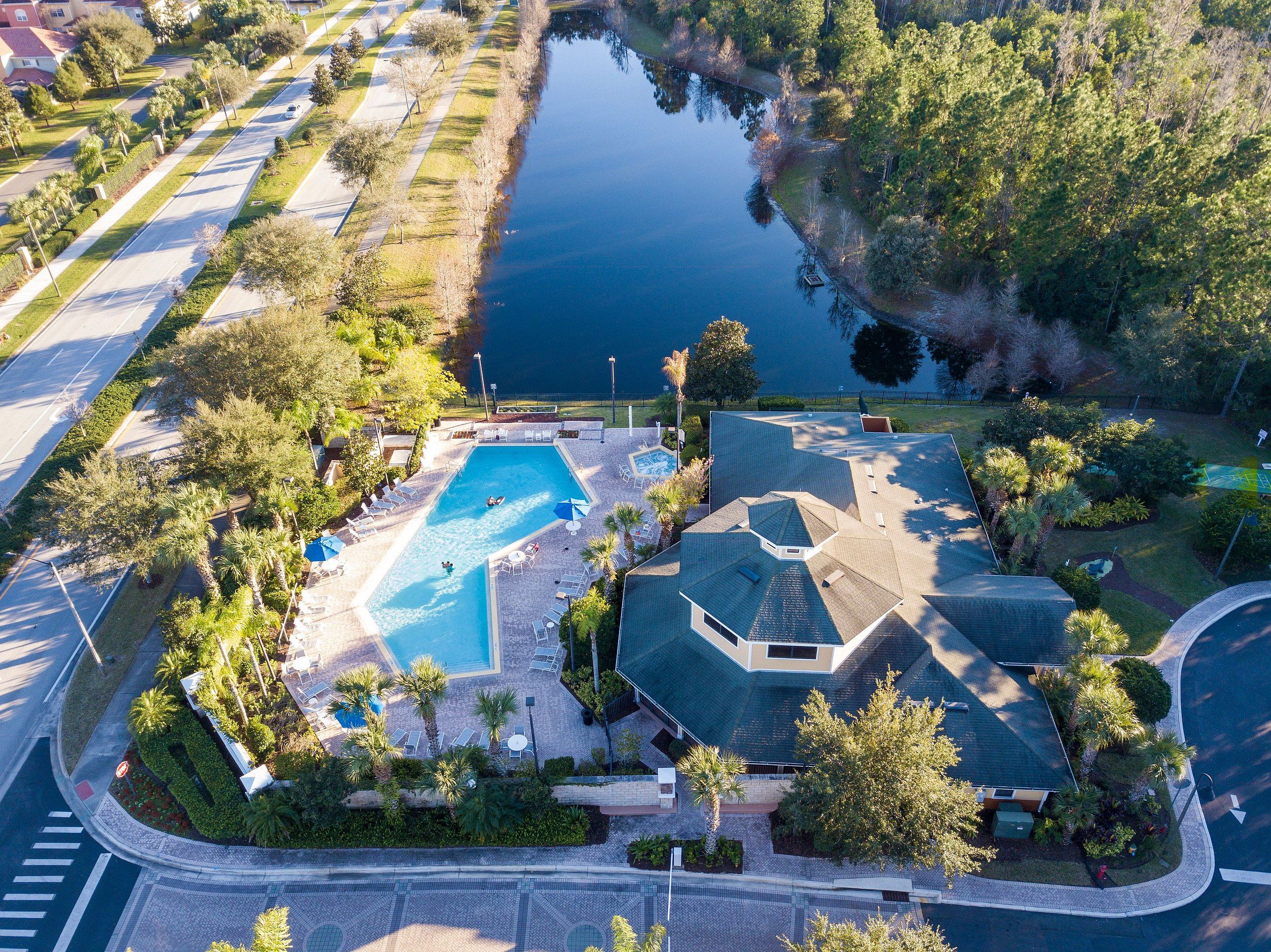 An aerial view of a residential area with a swimming pool, a tennis court, and a large house with a sloped roof.