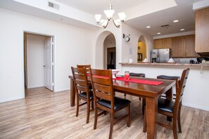 A dining area with a wooden table and chairs, a chandelier, and a kitchen in the background. - Modern Family Condo 15min From Disney (Kissimmee)