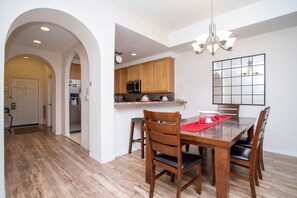 A dining area with a wooden table and chairs, a kitchen with wooden cabinets, and a chandelier. - Modern Family Condo 15min From Disney (Kissimmee)