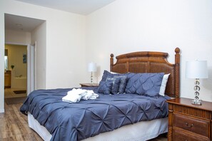 Un lit bien fait, recouvert d’une couverture bleu foncé, avec deux lampes de chevet et une table de chevet en bois dotée de tiroirs.