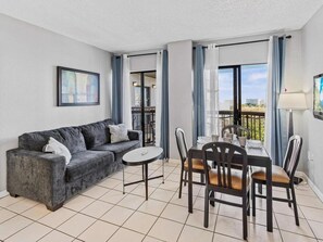 A modern living room with a grey sofa, a round table, and a dining set. - Cozy Retreat at The Enclave Suites (Orlando)
