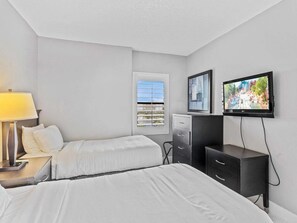 A hotel room with two beds, a TV, a desk with a lamp, a dresser, and a window with blinds. - Cozy Retreat at The Enclave Suites (Orlando)