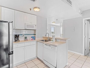 A modern kitchen with white cabinets, a stainless steel refrigerator, a microwave, a coffee maker, and a dishwasher. - Cozy Retreat at The Enclave Suites (Orlando)