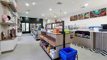 Una tienda limpia y ordenada, con estantes repletos de diversos productos, una cesta de compra azul y obras de arte en las paredes.