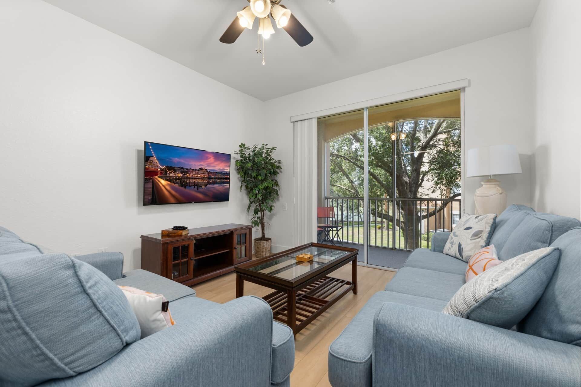 A living room with a flat-screen TV, a glass coffee table, and a sofa.