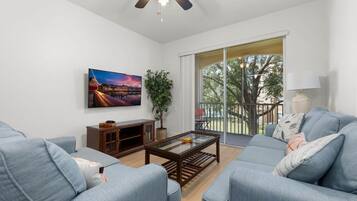 A living room with a flat-screen TV, a glass coffee table, and a sofa.