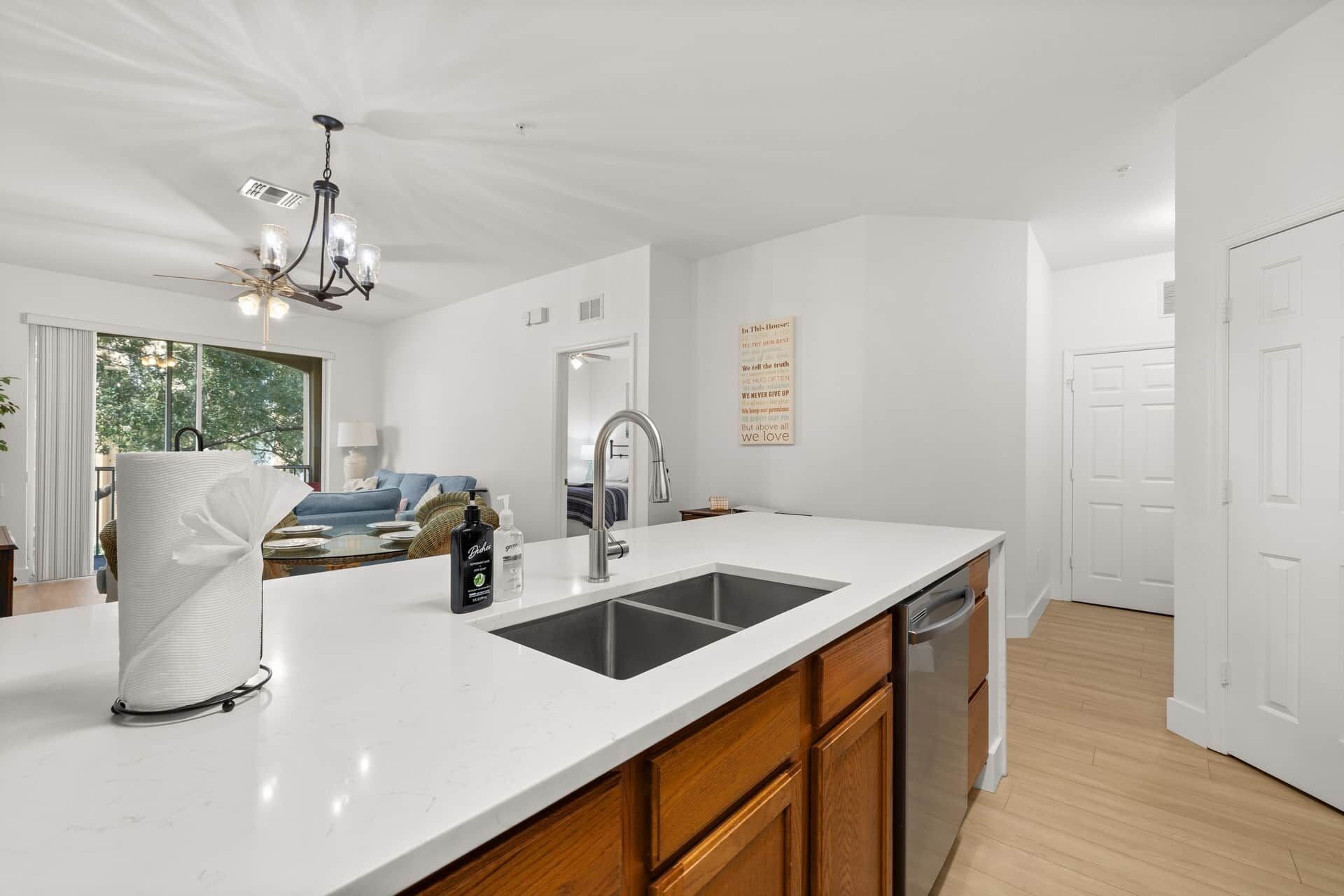 Una cocina moderna con encimera blanca, pileta de acero inoxidable y muebles de madera.