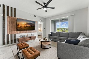 Een moderne woonkamer met een grote flatscreen-televisie, een grijze bank, een salontafel en een plafondventilator.