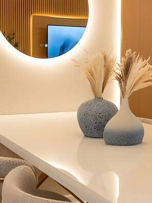 A modern interior with a curved white countertop, two stone vases with dried plants, and a television in the background. - Storey Lake 2BR Condo Lake & Clubhouse View (Kissimmee)