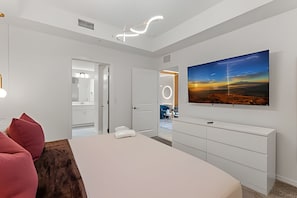 A modern bedroom with a large bed, a dresser, and a painting of a sunset. - Storey Lake 2BR Condo Lake & Clubhouse View (Kissimmee)