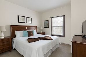 A bedroom with a wooden bed, white bedding, a brown throw blanket, a nightstand with a lamp, a dresser, and a television on a stand. - Disney 3BR Townhome w/ Pool & Mickey Theme (Kissimmee)