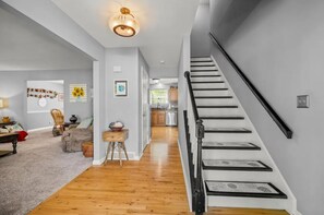 A modern interior with a staircase, wooden flooring, and a kitchen in the background. - ZEN ON O'RYAN  5 BEDROOM HOUSE IN OXFORD OHIO (Oxford)