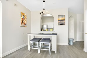 A modern kitchen with a central island, two stools, a chandelier, and artwork on the walls. - Disney 3BR Retreat at Windsor Palms Resort (Kissimmee)