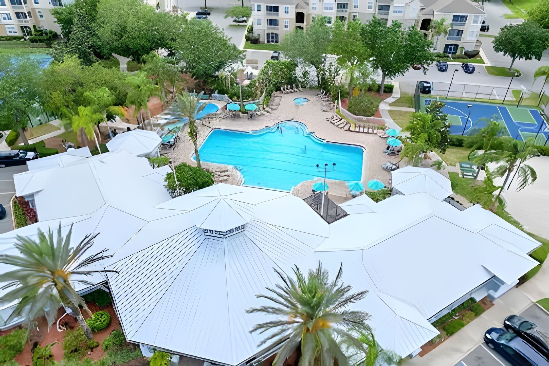 A residential building with a swimming pool, covered outdoor seating, and palm trees.