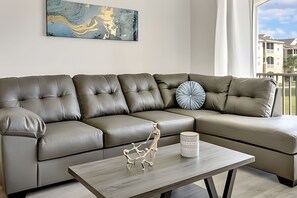 A modern living room with a grey leather sectional sofa, a white coffee table with a sculpture, and a blue abstract painting on the wall. - Disney 3BR Retreat at Windsor Palms Resort (Kissimmee)