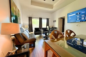 A modern living room with a sofa, a dining table, and a TV mounted on the wall. - Seven Eagles 3BR Condo Across From Reunion Grande (Kissimmee)