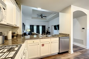 A modern kitchen with white cabinetry, a granite countertop, and a built-in dishwasher. - Seven Eagles 3BR Condo Across From Reunion Grande (Kissimmee)