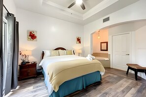 A hotel room with a bed, bedside tables, a nightstand, a bench, a door, and a ceiling fan. - Seven Eagles 3BR Condo Across From Reunion Grande (Kissimmee)