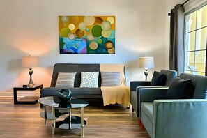 A modern living room with a sofa, a coffee table, and a painting on the wall. - Seven Eagles 3BR Condo Across From Reunion Grande (Kissimmee)