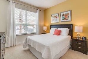 A neatly arranged bedroom with a large bed, two bedside tables with lamps, a dresser, and a window with blinds. - Serenity 3BR Villa w/ Pool Near Disney (Clermont)