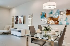 A modern dining area with a glass table, white chairs, and a contemporary painting. - Serenity 3BR Villa w/ Pool Near Disney (Clermont)