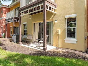 A two-story house with a covered patio, a sliding glass door, and a small outdoor seating area. - 3BR Villa in Emerald Island Near Disney (Kissimmee)