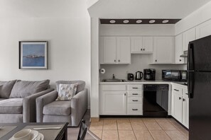 A compact kitchen with white cabinets, a black refrigerator, and a coffee maker. - Pool View Suite Near Disney, 1BR Comfort (Orlando)