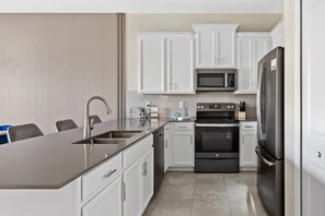 A modern kitchen with white cabinets, a stainless steel refrigerator, a microwave, and an oven. - 2BR Golf View Condo + Champions Gate Resort (Davenport)