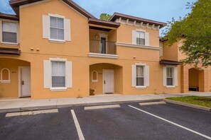 Um edifício residencial de vários andares com telhado plano, persianas brancas e uma varanda no segundo pavimento.